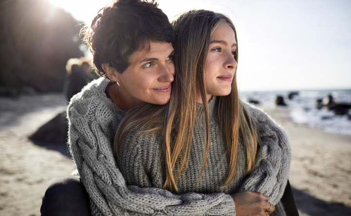 A mother wrapping her arms around her daughter from behind at the beach