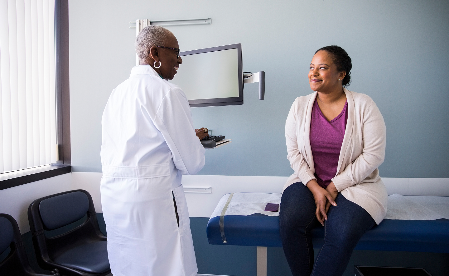 A doctor talking to her female patient who is sitting on a medical examination table