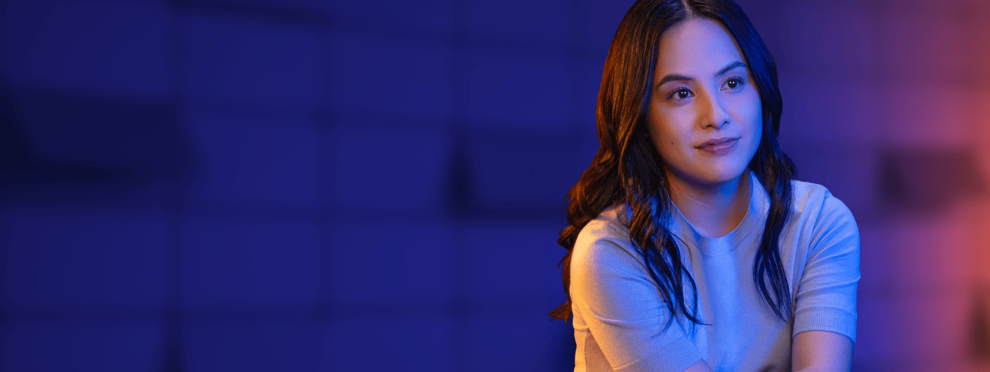 A woman posing with her arms crossed on her knee in front of a backdrop that reads "SEIZE YOUR WHEN"