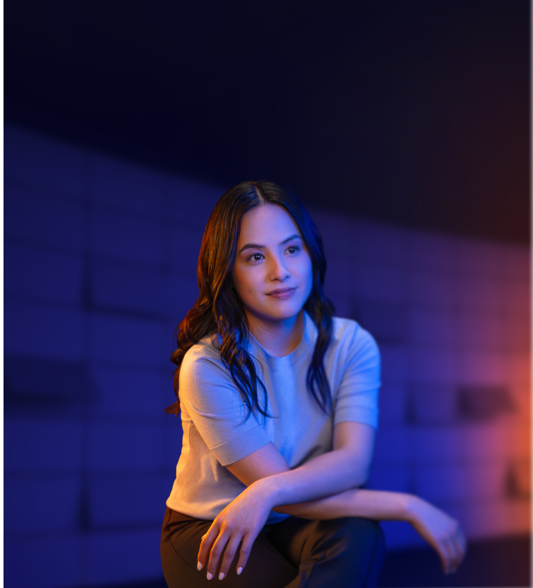 A woman posing with her arms crossed on her knee in front of a backdrop that reads "SEIZE YOUR WHEN"