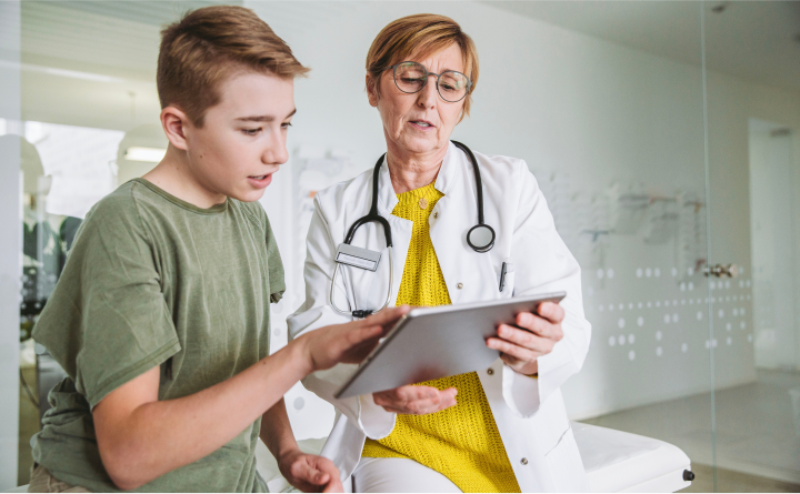 A doctor speaking with a young boy and showing him her tablet
