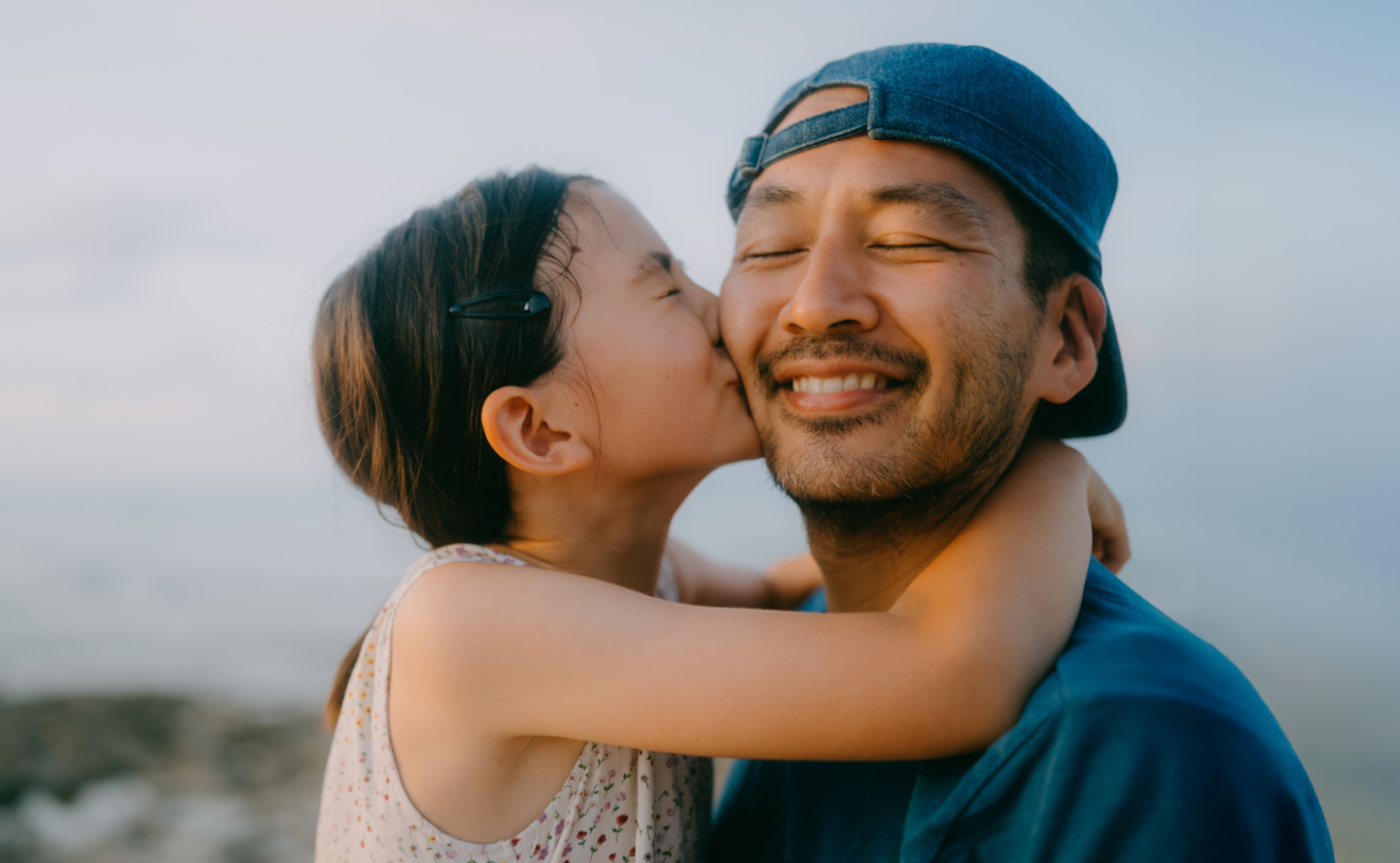 A young daughter wrapping her arms around her father's neck and giving him a kiss on the cheek