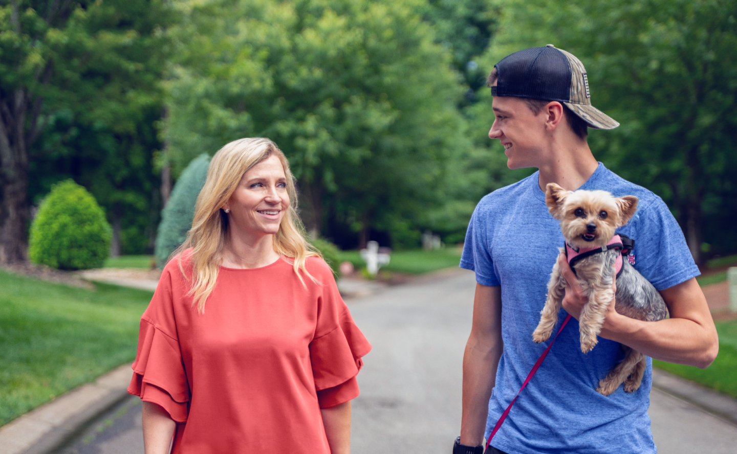 William, a TZIELD® (teplizumab-mzwv) patient, holding a small dog while walking outdoors with his mother and caregiver, Amanda