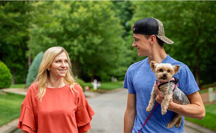 William, a TZIELD® (teplizumab-mzwv) patient, holding a small dog while walking outdoors with his mother and caregiver, Amanda