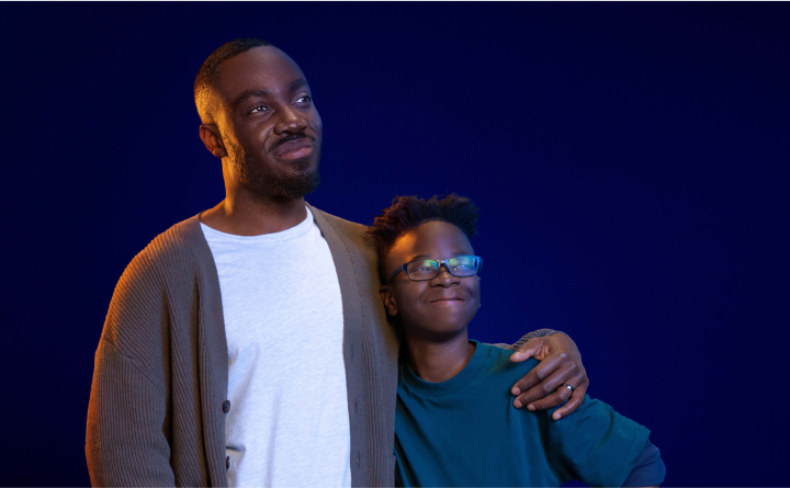 A father with his arm wrapped around his son and both are smiling into the distance